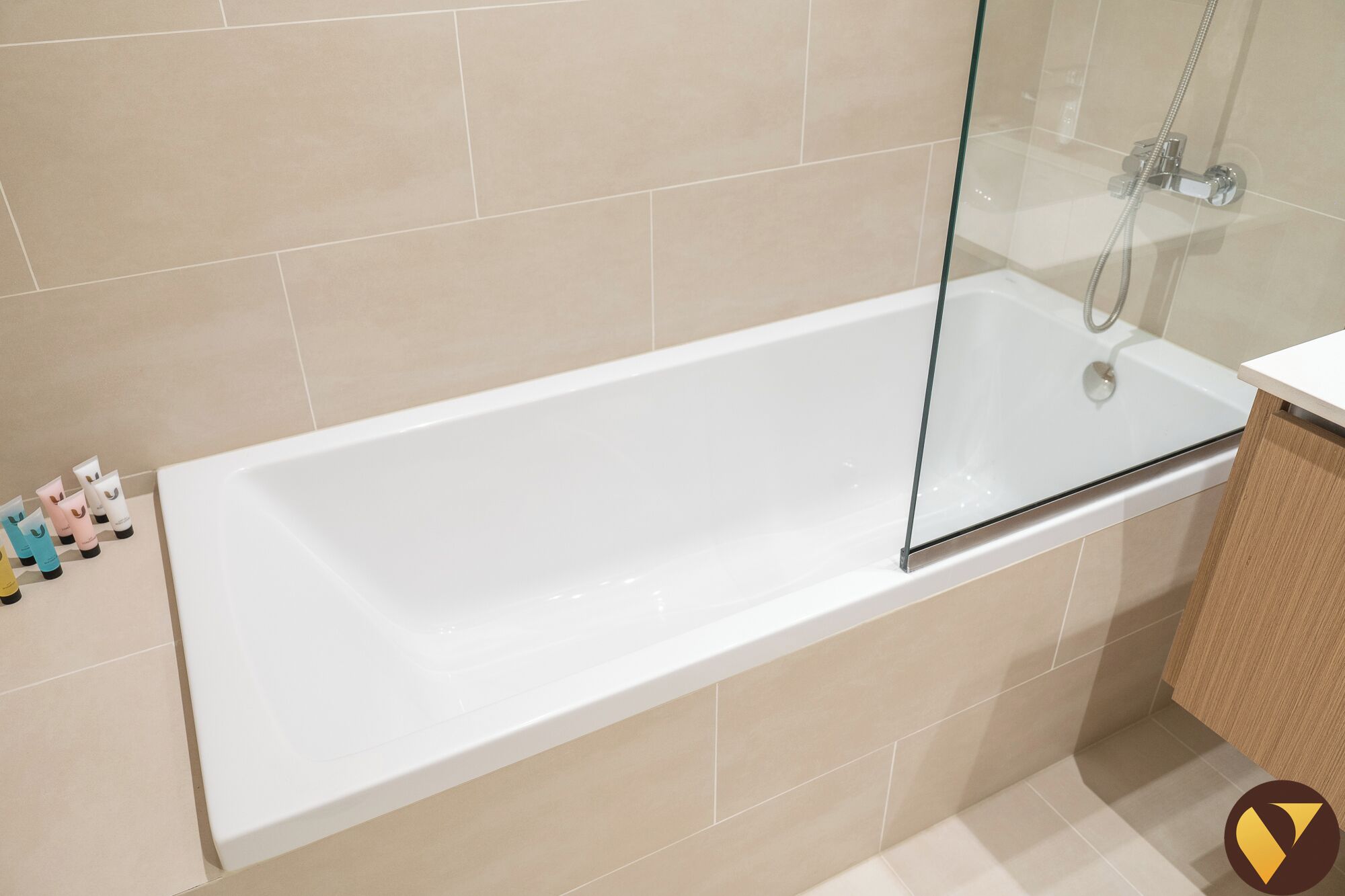 Un bagno moderno con vasca da bagno vetrata, piastrelle color beige e zona doccia a vista.