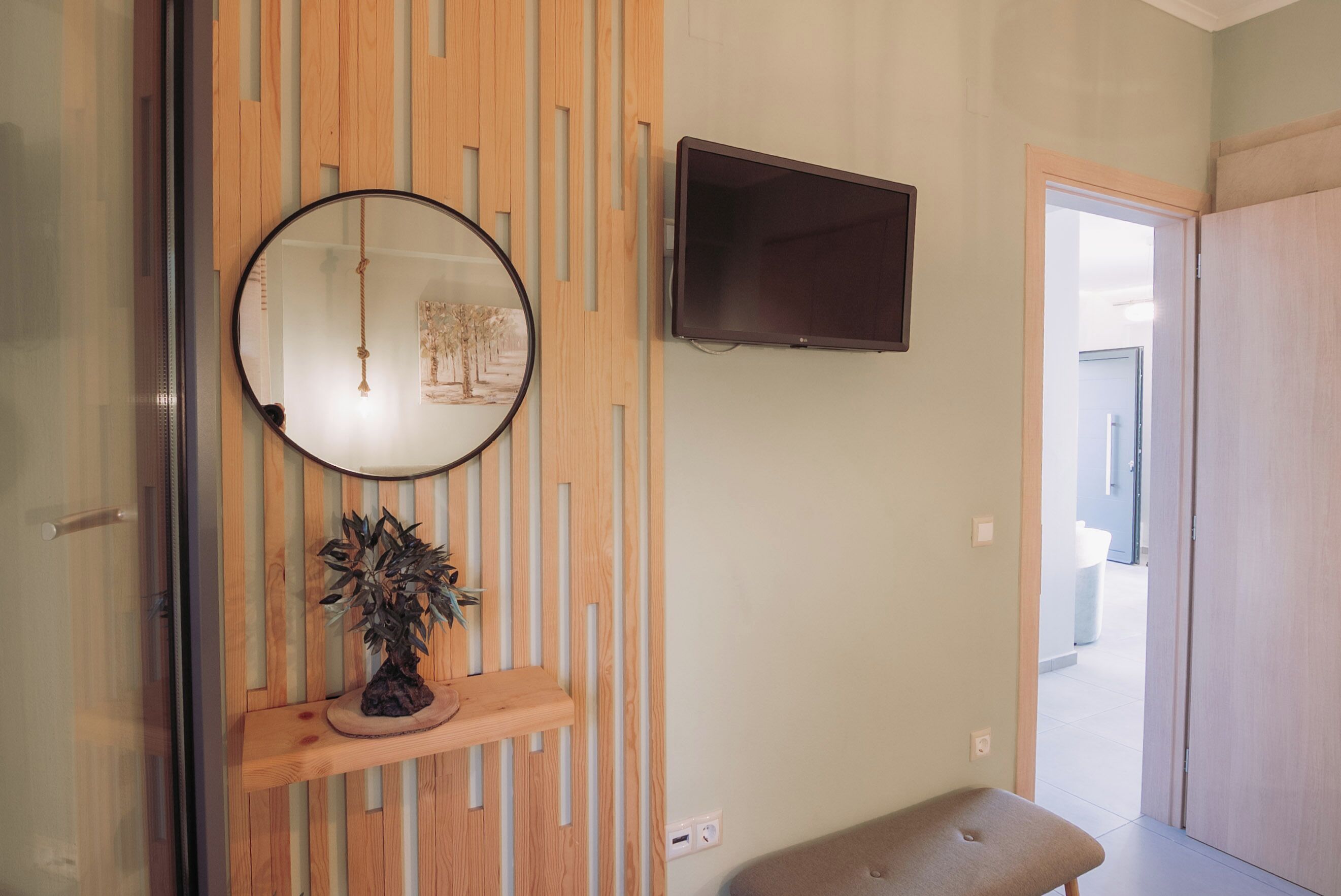 A room with a wooden slat wall, a round mirror, a flat-screen TV, and a bench.