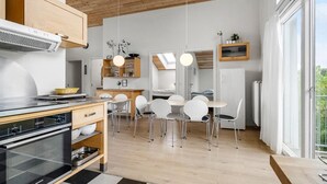Eine moderne Küche mit Einbauofen, ein Essbereich mit weißen Stühlen und ein großes Fenster für natürliches Licht.