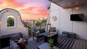 Une terrasse sur le toit offrant une vue sur la ville, des sièges d’extérieur, un téléviseur à écran plat et des guirlandes lumineuses.