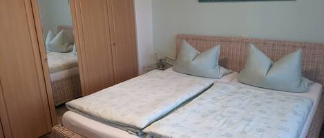 A double bed with a patterned duvet, a wicker headboard, and a painting on the wall.