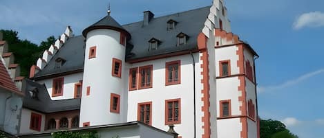 A castle-like building with multiple towers and a turret, featuring a mix of white and red walls, and a grey roof.