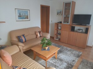 Un salon comprenant un canapé, une table basse avec une plante, un téléviseur posé sur un meuble en bois et une bibliothèque.