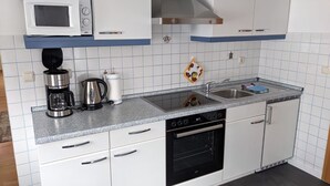 A kitchen with white cabinets, a microwave, a coffee maker, a kettle, a sink, and an oven.
