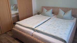 A double bed with a patterned duvet, a wicker headboard, and a painting on the wall.