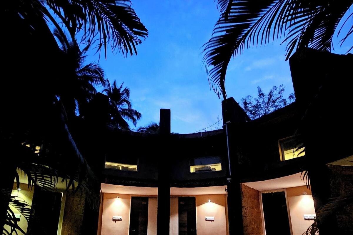 A circular outdoor area with a brick floor, surrounded by palm trees and walls with illuminated windows.
