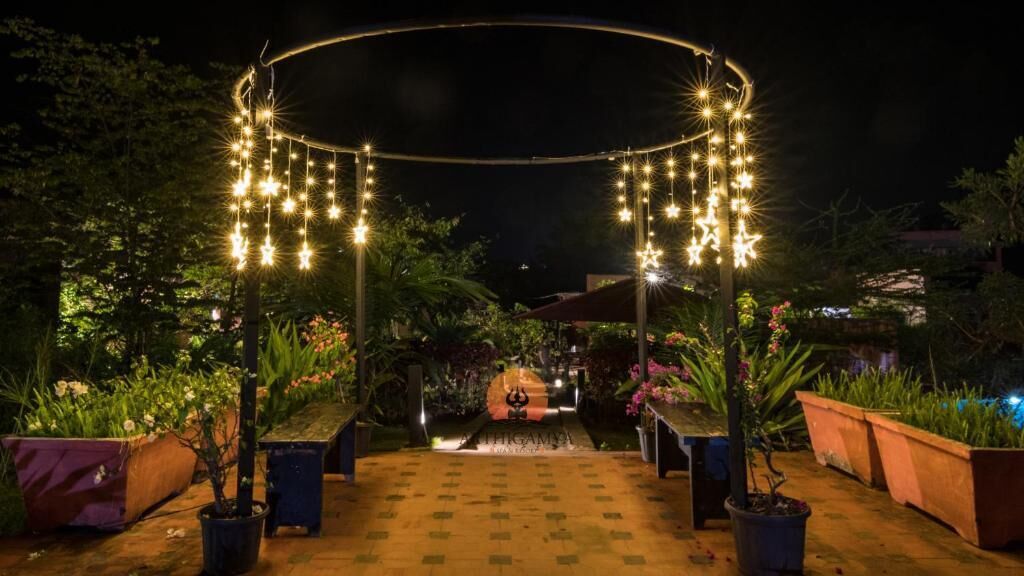An outdoor garden pathway with a circular archway adorned with string lights and star-shaped decorations.