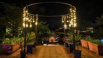 An outdoor garden pathway with a circular archway adorned with string lights and star-shaped decorations.
