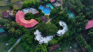 Vue aérienne d’un complexe hôtelier comprenant plusieurs bâtiments de forme circulaire, une piscine et des palmiers environnants.