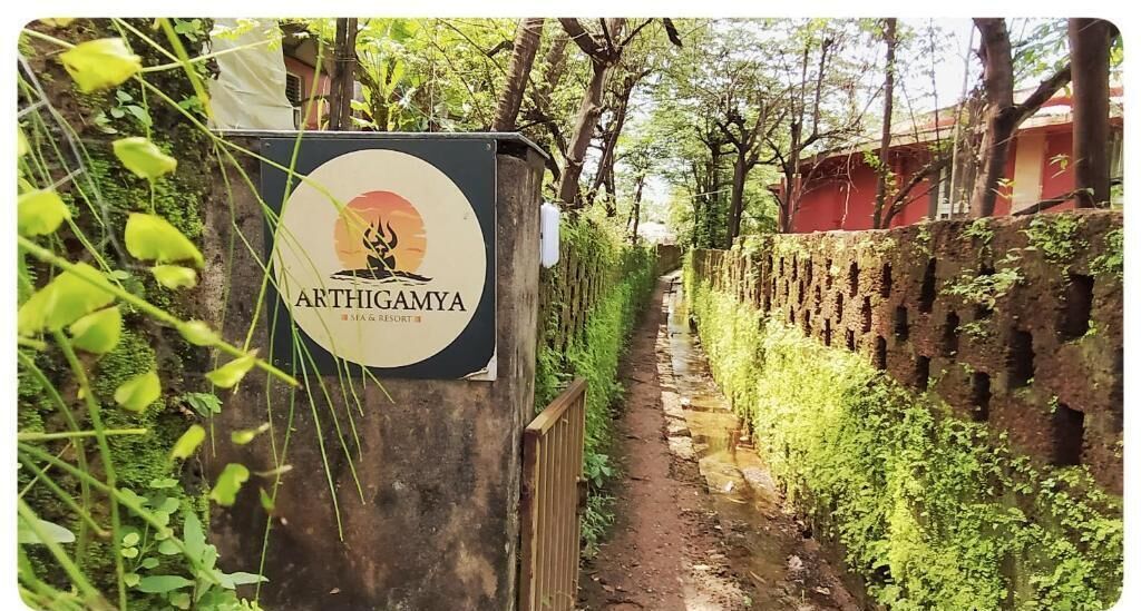 Ein Schild für Arthigaya, ein Spa und Resort, mit einem Weg, der durch eine üppige, grüne Landschaft führt.