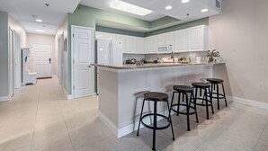 A modern kitchen with white cabinets, a granite countertop, and four bar stools. - Resort-style 3BR condo near the beach with pools, tennis, sauna, gym & great location. (New Smyrna Beach)