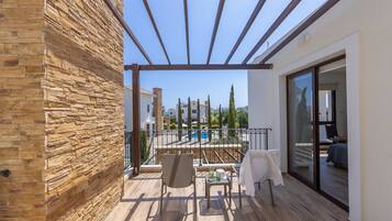 A balcony with a pergola, a pool in the background, and a view of other buildings.