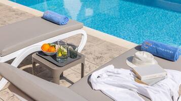 A poolside lounge area with a table set with a drink, fruit, and a book.