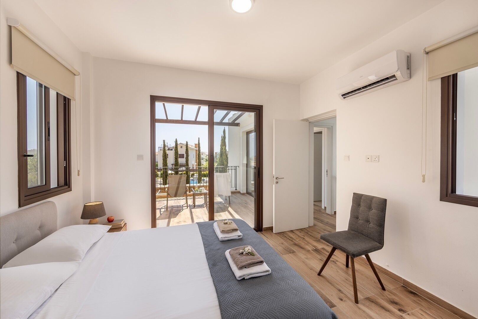 A bedroom with a bed, a chair, and a view of a pool and buildings outside.