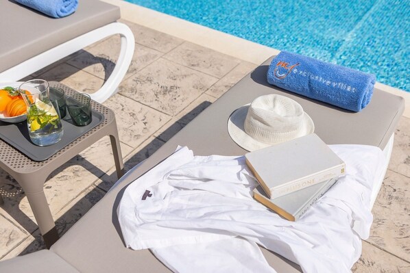 Un área de descanso junto a la piscina, con una mesa, un sombrero, un libro y una toalla.