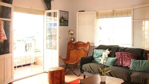 Una sala de estar con un sofá, una silla de madera, una mesa con una planta y una ventana con persianas.