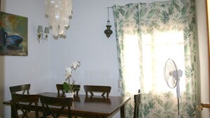 Un comedor con una mesa y sillas de madera, una lámpara colgante, una lámpara de pared y un ventanal con cortinas.