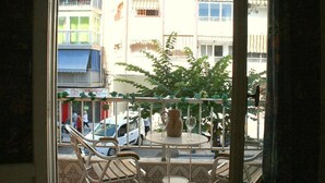 Un balcón con mesa y sillas, con vista a una calle con edificios y coches aparcados.