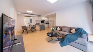 Een moderne woonkamer met een bank, salontafel, televisie en een eethoek met stoelen en een tafel.