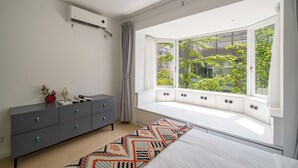Een slaapkamer met een groot raam, een bed, een nachtkastje en een kast.