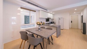 Een moderne keuken met een centraal eiland, een eethoek met tafel en stoelen, en uitzicht op de straat door grote ramen.