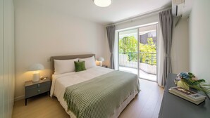 Een slaapkamer met een bed, nachtkastjes, een raam met gordijnen en uitzicht op groen buiten.