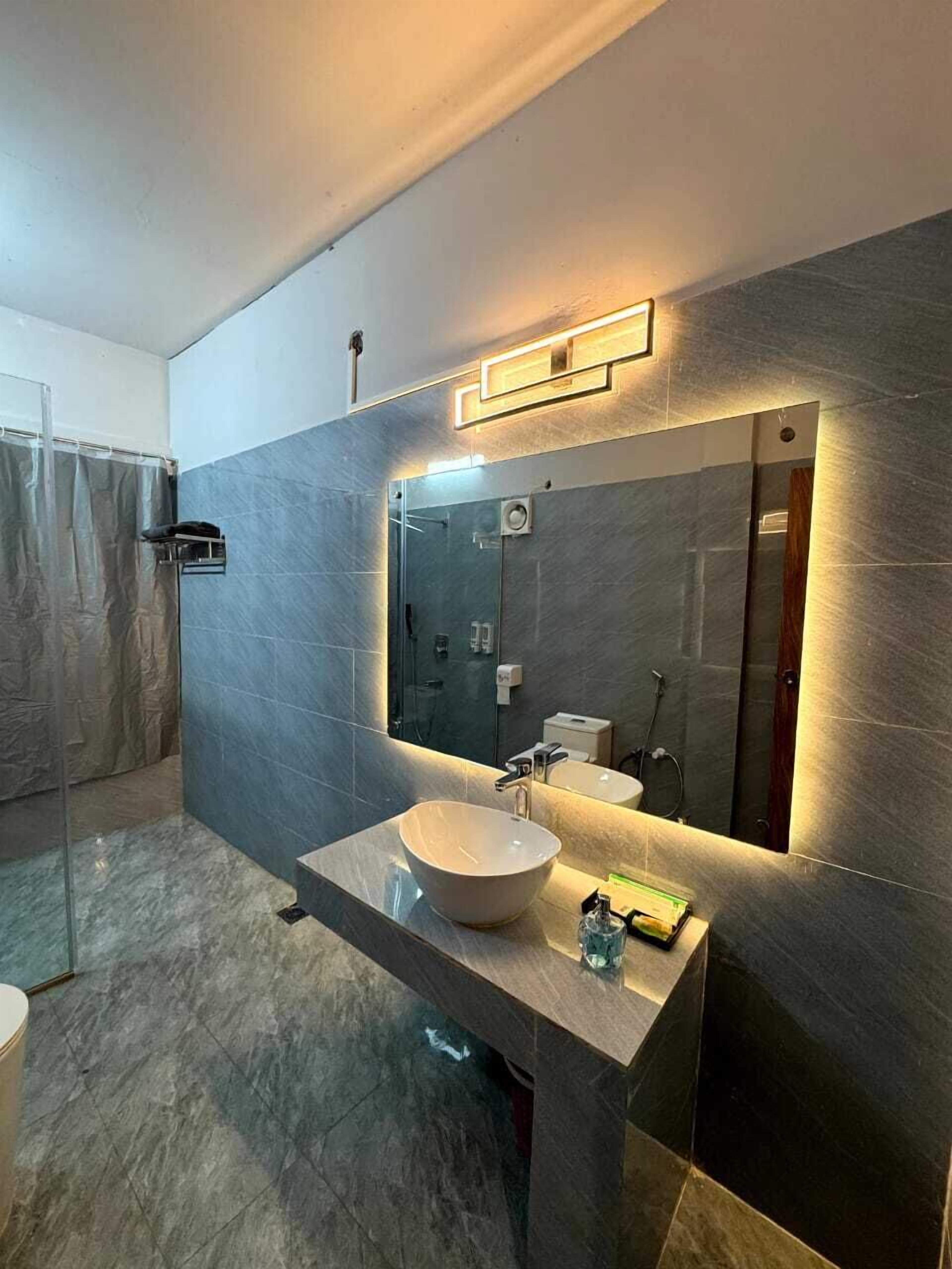 Un baño moderno con un espejo grande, un lavabo tipo recipiente y una zona de ducha.