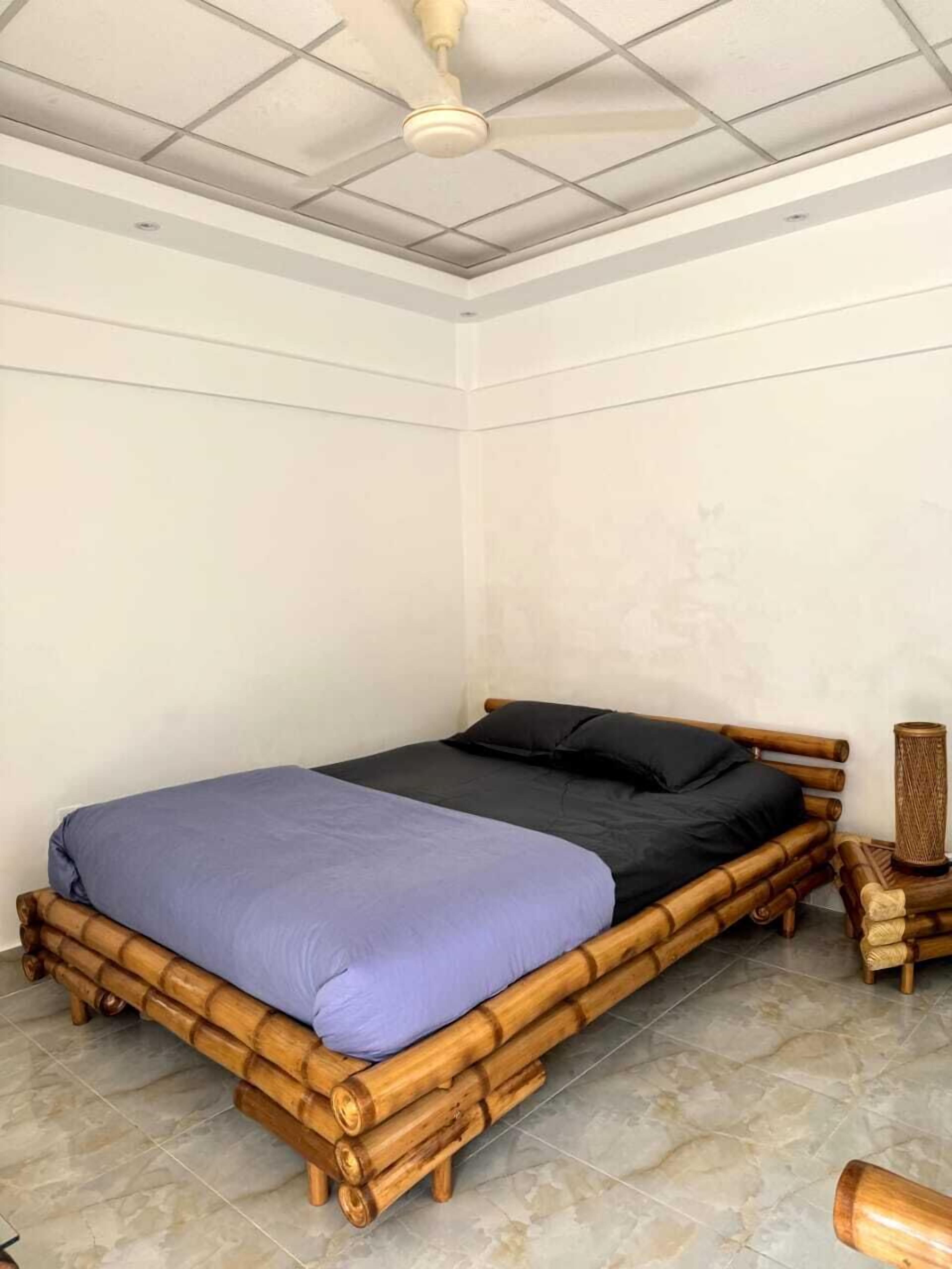 A room with a bamboo bed frame, a purple bedspread, and a wooden nightstand with a cat scratching post.