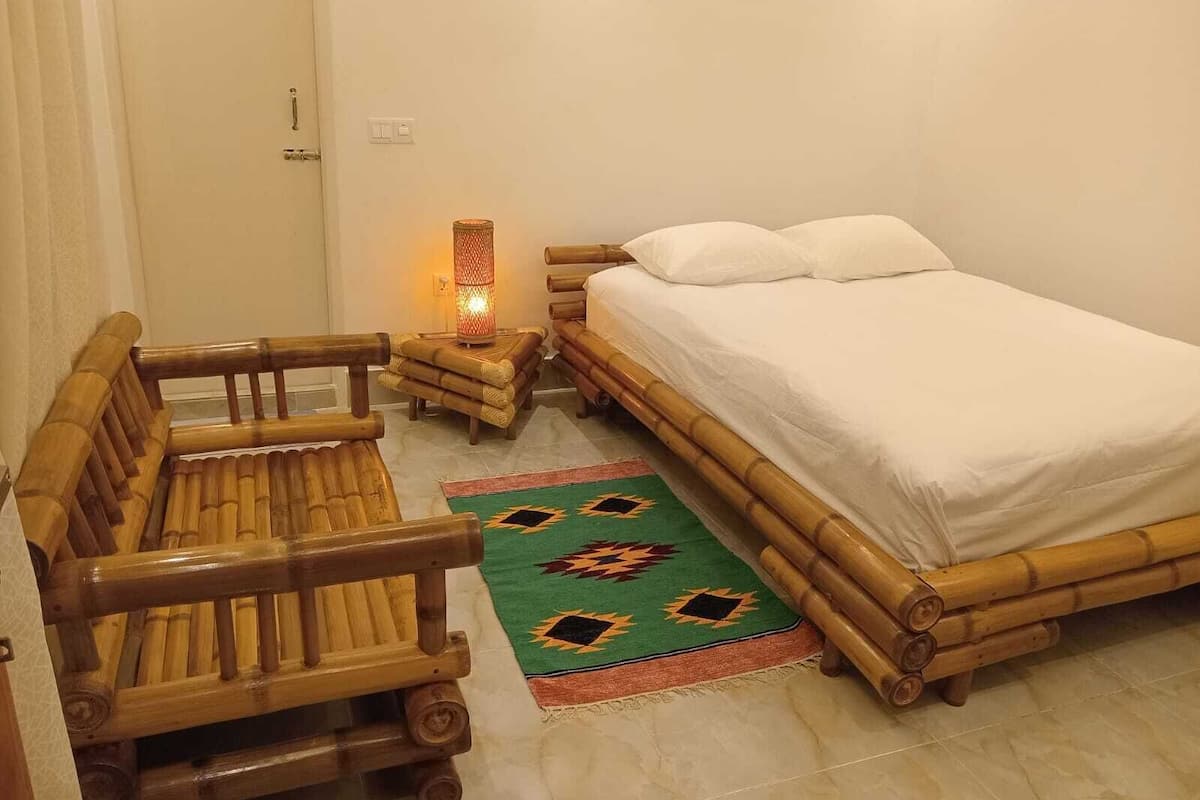 Ein Zimmer mit einem Bett, einer hölzernen Bank, einem kleinen Tisch mit einer Lampe und einem gemusterten Teppich.