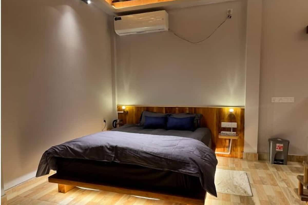 Ein Schlafzimmer mit Bett, Holz-Kopfstück, Nachttischen und einer Klimaanlage.