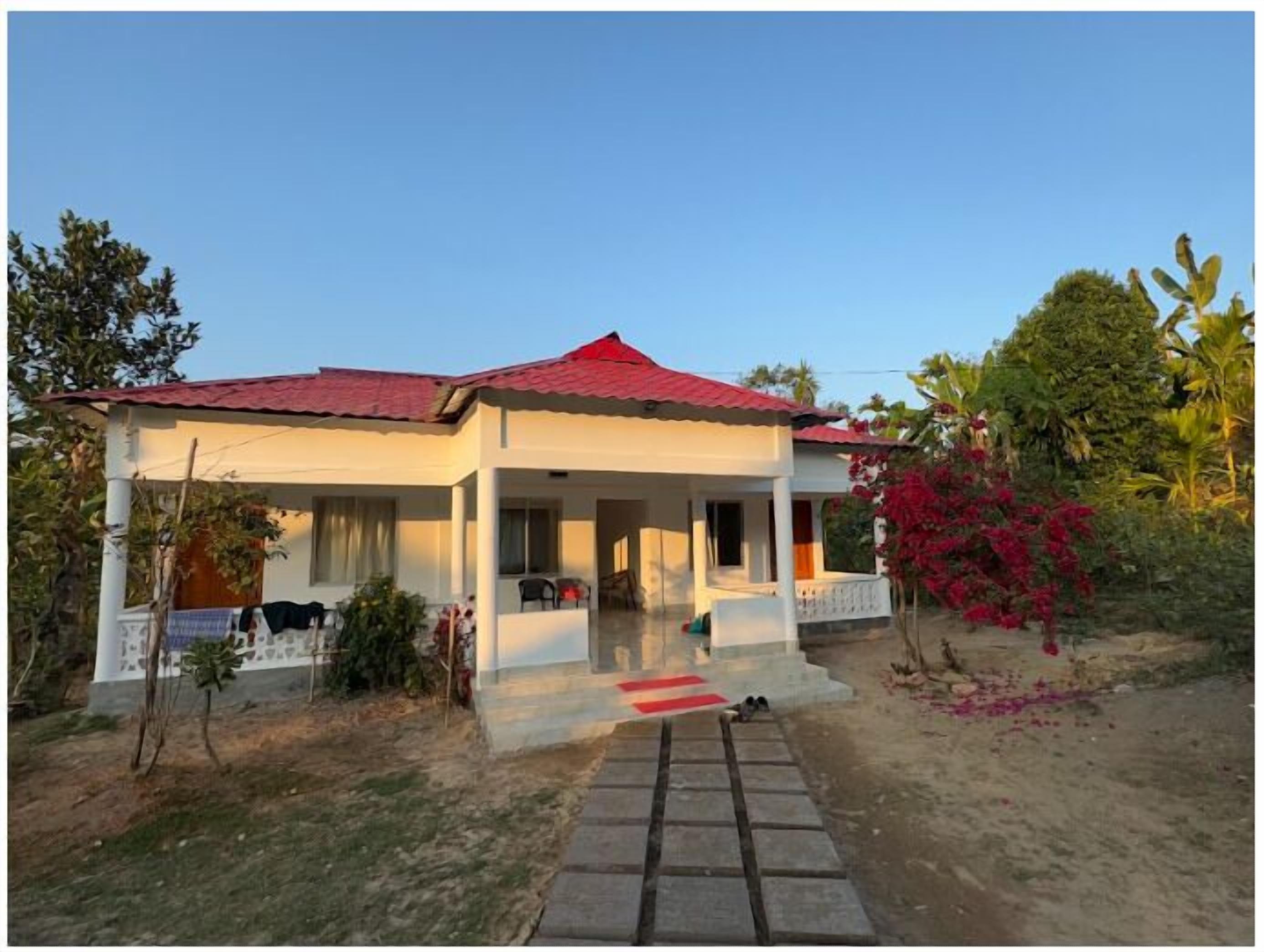 A two-story house with a red roof, a covered porch, and a small garden area with red flowers.