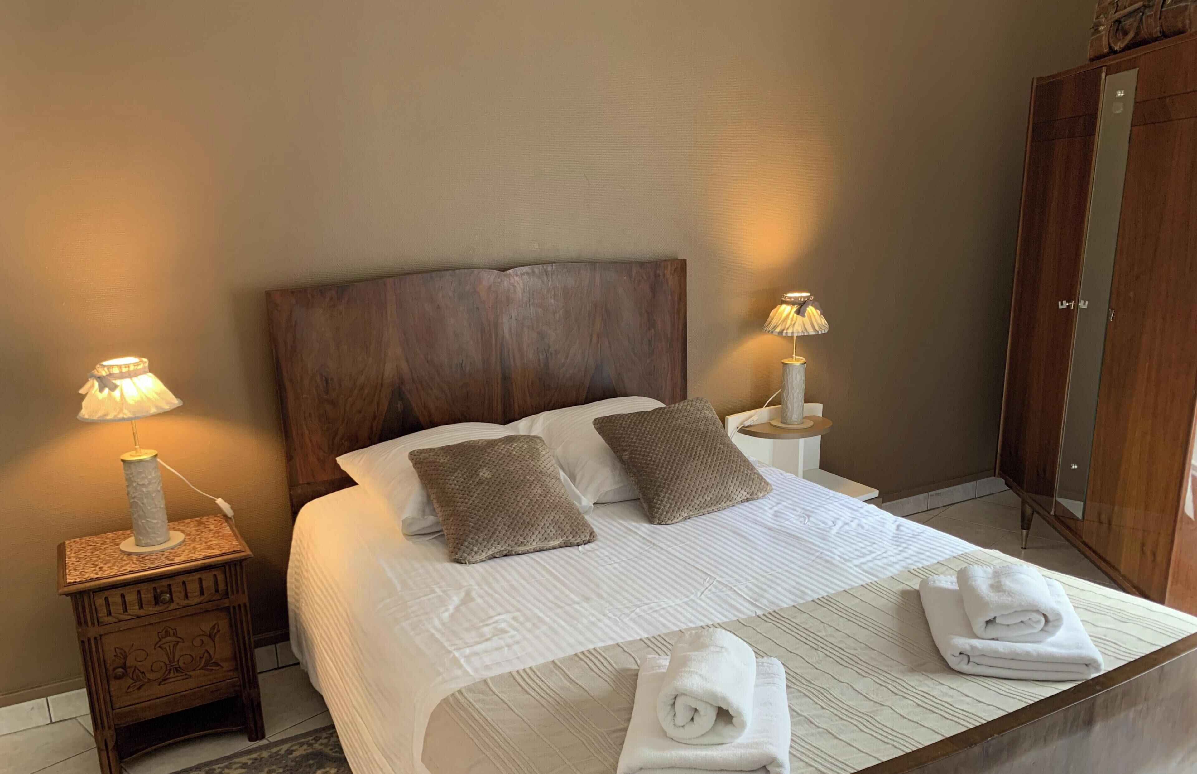 A neatly made bed with two pillows, a nightstand with a lamp, and a wooden wardrobe.