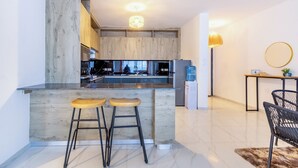 A modern kitchen with a marble countertop, wooden bar stools, and a dining area with a round table and chairs. - Spacious Loft in Lavington With Pool + Gym & Playground (Nairobi)