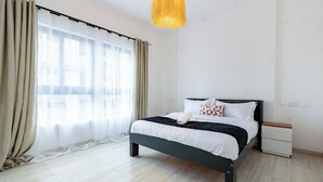 A modern bedroom with a bed, bedside tables, and a large window with curtains. - Spacious Loft in Lavington With Pool + Gym & Playground (Nairobi)