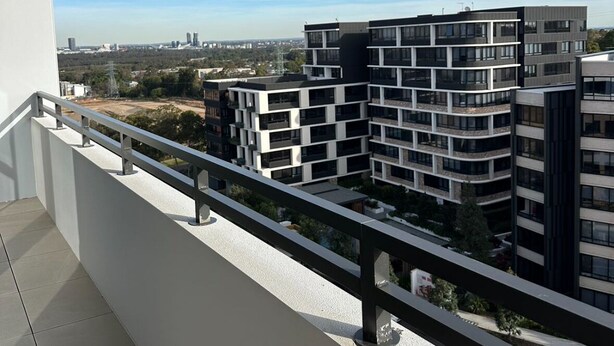 Ein Balkon mit Blick auf moderne Wohngebäude, einen klaren Himmel und eine entfernte Stadtlandschaft.