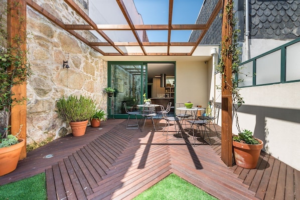 A patio with wooden flooring, potted plants, and a glass door leading to a kitchen area.