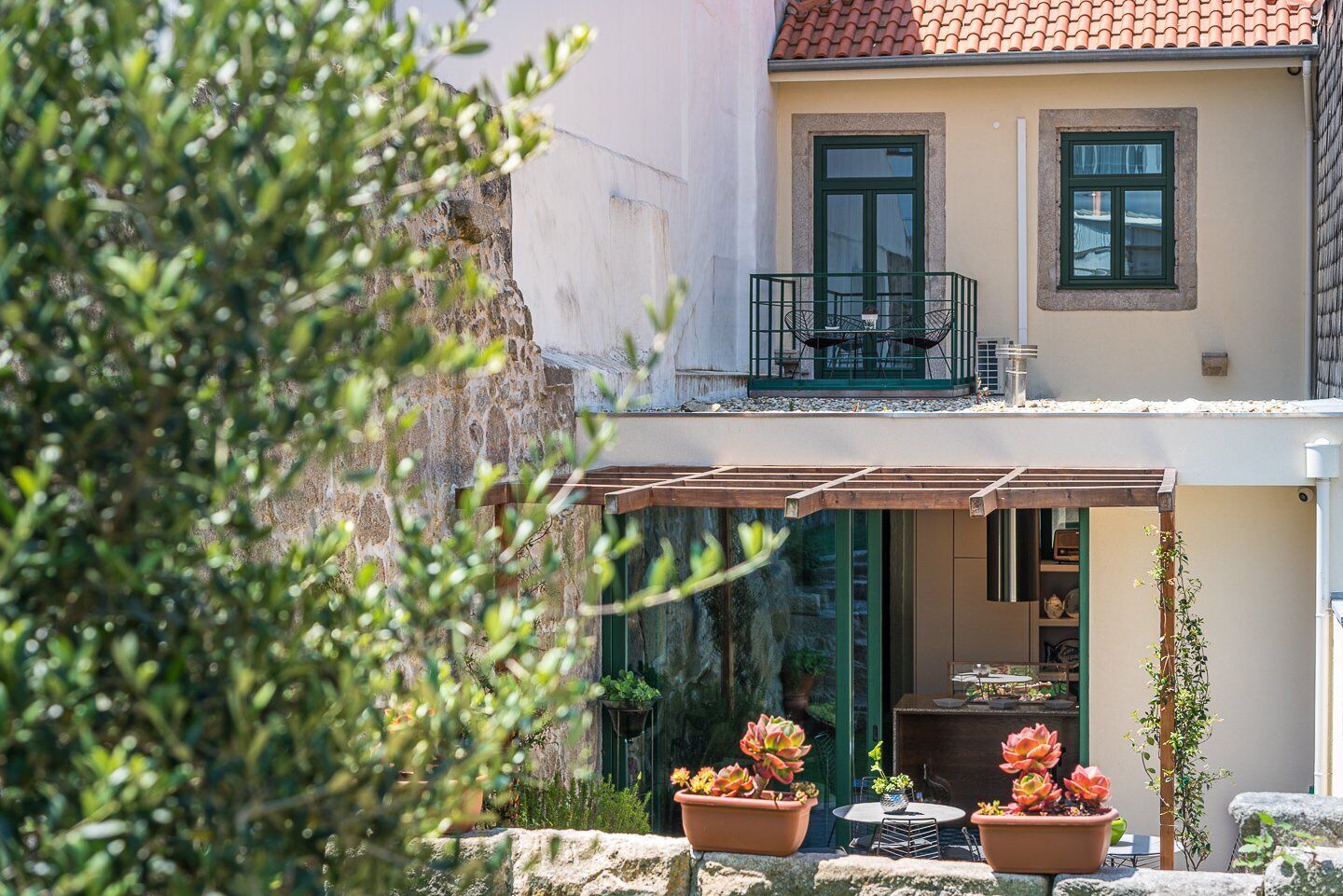 Ein zweistöckiges Gebäude mit Balkon, Sitzgelegenheiten im Freien und Pflanzkübeln.