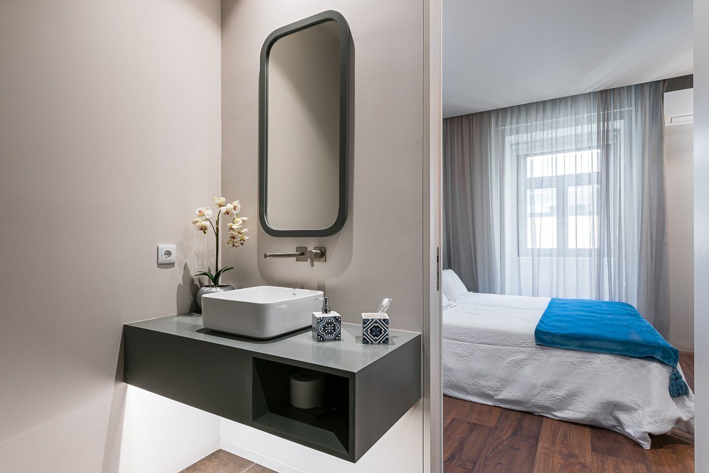 Un baño moderno con un espejo grande, un lavamanos blanco y una pequeña florera con flores.