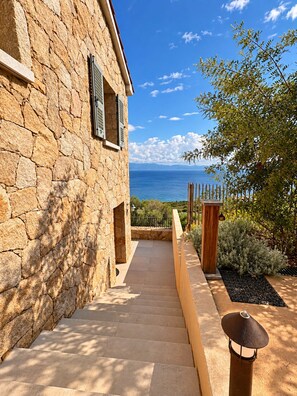 A stone building with a view of the sea, a paved pathway, and a wooden gate.