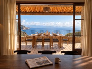 A dining area with a table set for four, overlooking a scenic view of the sea and mountains.