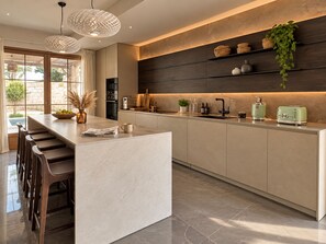 A modern kitchen with a central island, bar stools, pendant lighting, and a built-in oven.
