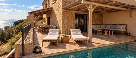 Una casa de piedra con piscina, zona de estar al aire libre y vistas al mar.