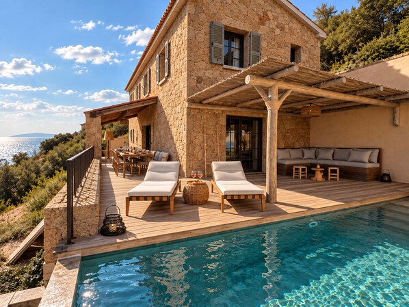 A stone house with a pool, outdoor seating, and a view of the sea.