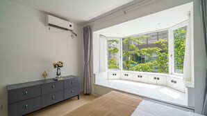 Un dormitorio con un ventanal grande, una cama, un aparador y un aire acondicionado instalado en la pared.