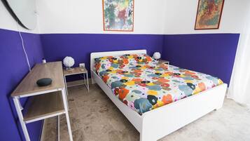 Un dormitorio con una cama blanca, un escritorio de madera y una pared morada.