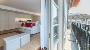 Ein modernes Wohnzimmer mit Sofa und Hocker, einer Küchenzeile und einem Balkon mit Geländer.