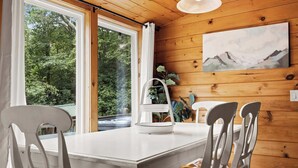 Una habitación con paneles de madera, una mesa de comedor y sillas, una ventana con vistas a árboles, y un cuadro en la pared.
