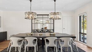 A modern dining area with a large table, white chairs, and hanging crystal chandeliers.