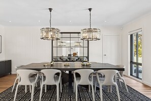 A modern dining area with a large table, white chairs, and hanging crystal chandeliers.