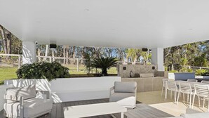 Un patio al aire libre con techo blanco, chimenea de piedra y una zona de estar que incluye un sofá, sillas y una mesa.